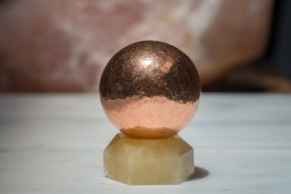Small copper sphere stone from Sacred Light Soundbaths and Crystals, showing a polished metallic finish and smooth surface.
