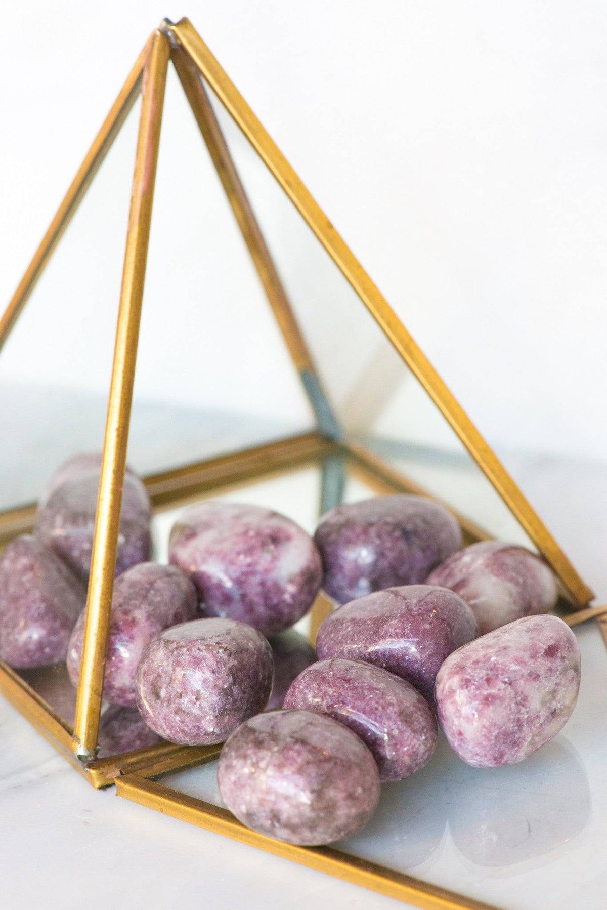 Tumbled Lepidolite stone from Sacred Light Soundbaths and Crystals, smooth purple mineral with layered, shiny surface.